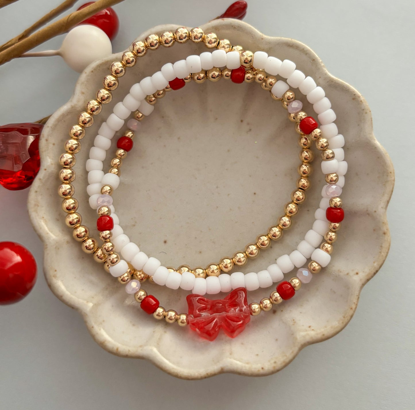 Beaded bracelets with gold, white, and red beads on a ceramic dish.