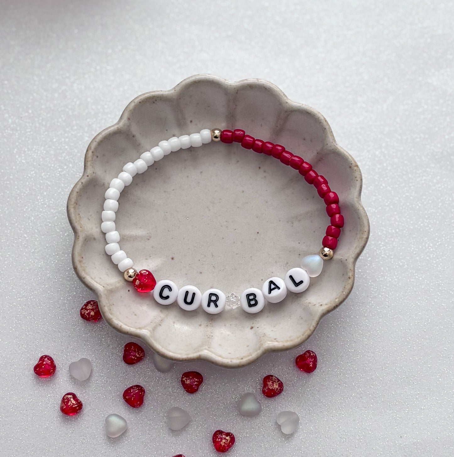 Beaded bracelet with letter beads spelling 'CURBAL' on a textured surface with scattered beads.