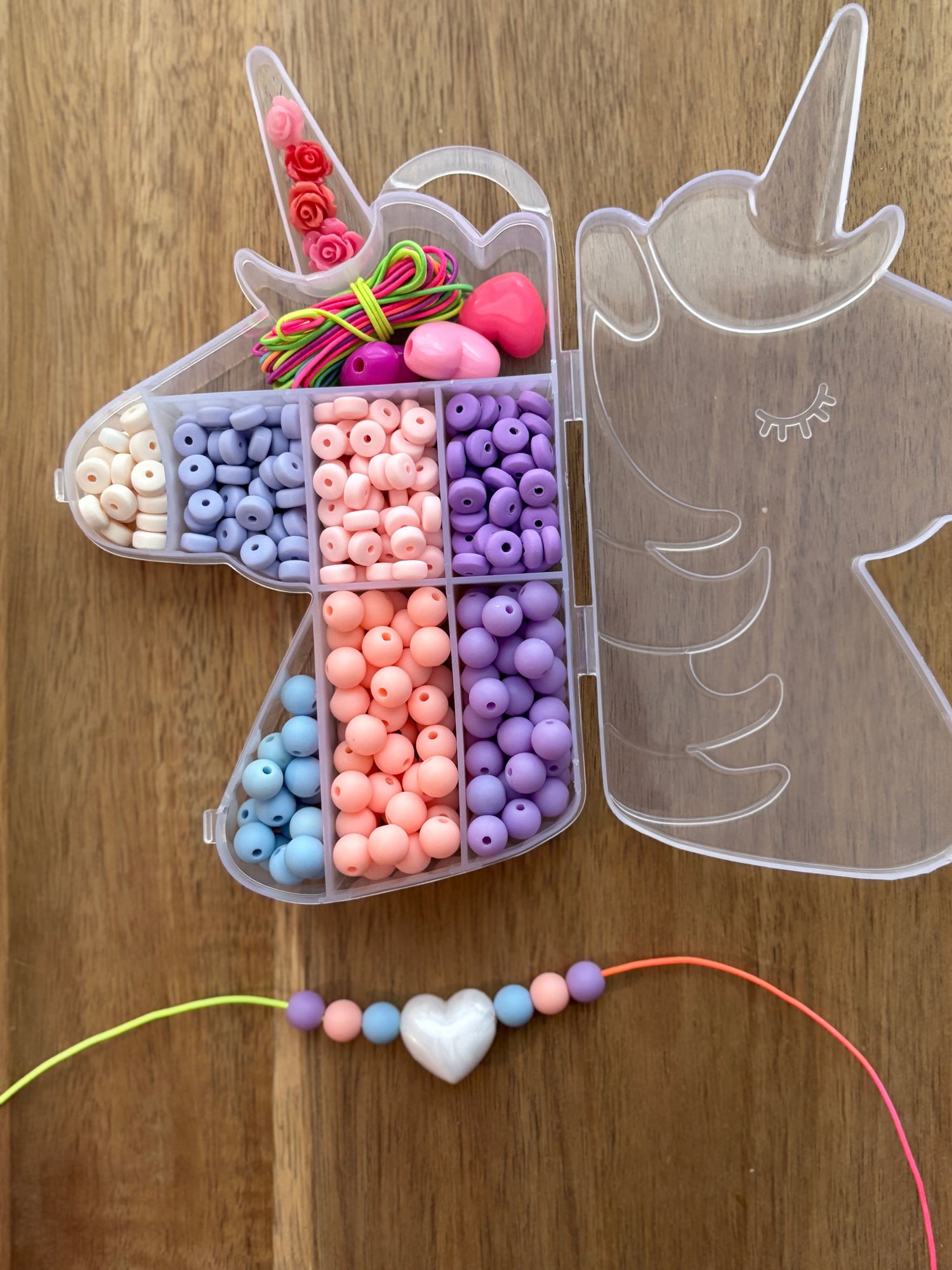 Unicorn-shaped bead kit with colorful beads and a made necklace on a wooden surface.