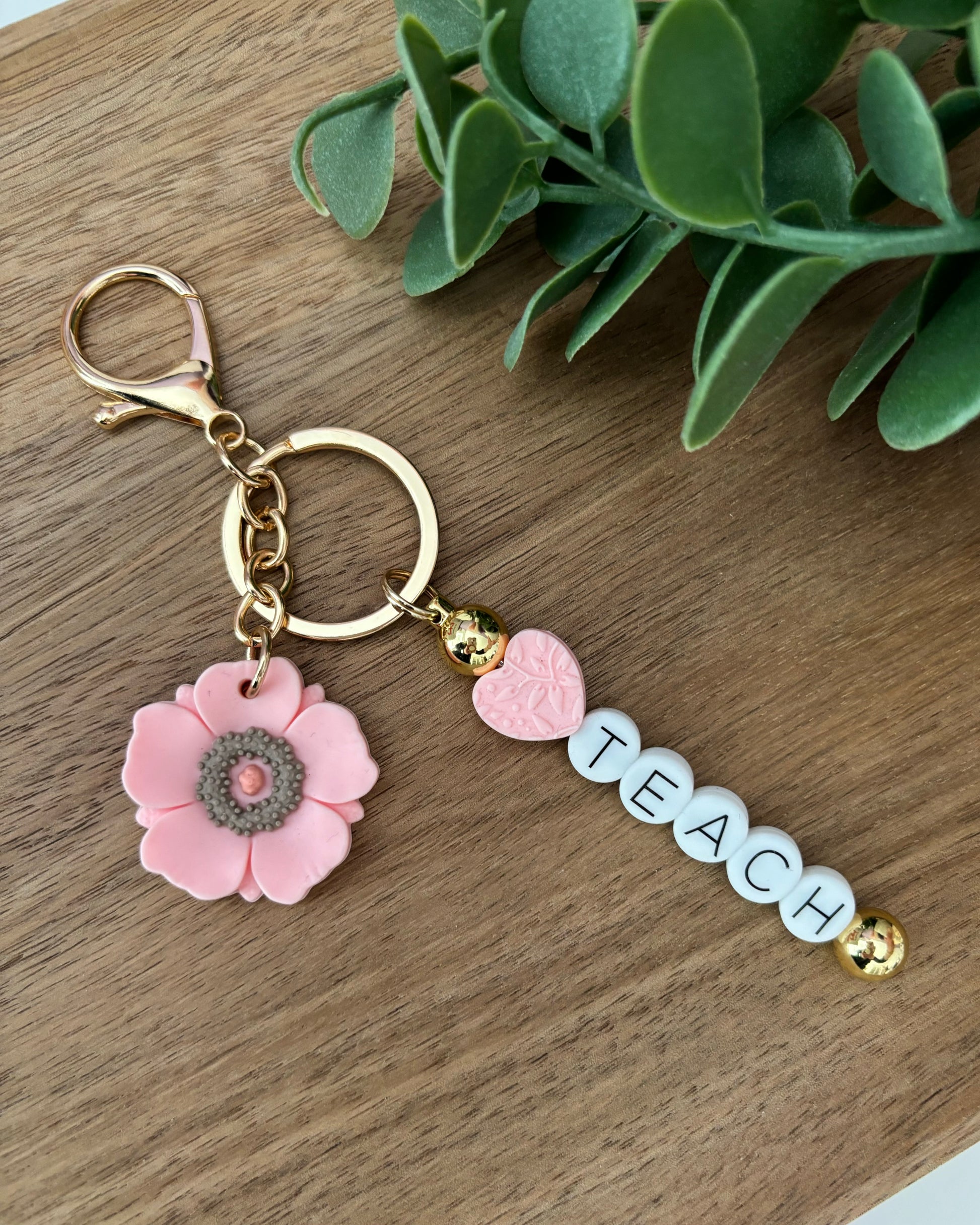 A keychain with a floral design and the word 'Teach' written on it, displayed on a wooden surface.