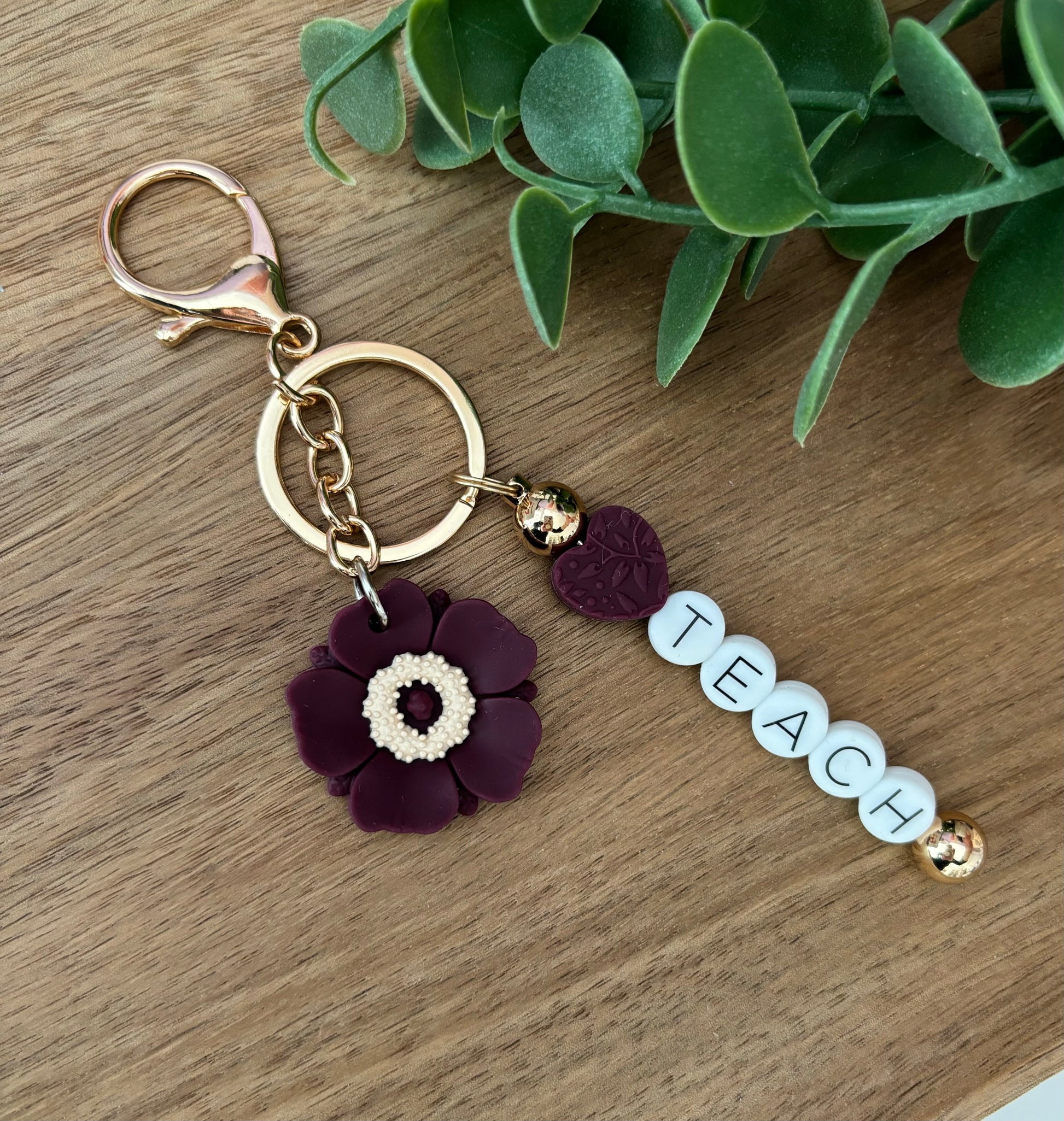 A keychain with a floral design and the word 'Teach' written on it, displayed on a wooden surface.