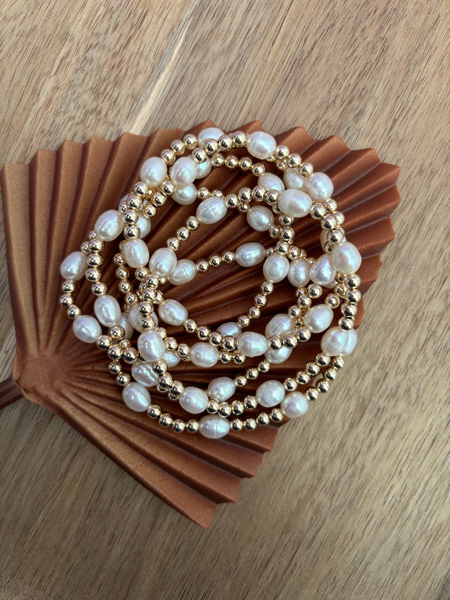 A bracelet with a combination of gold-filled and freshwater pearl beads, displayed on a brown paper surface.