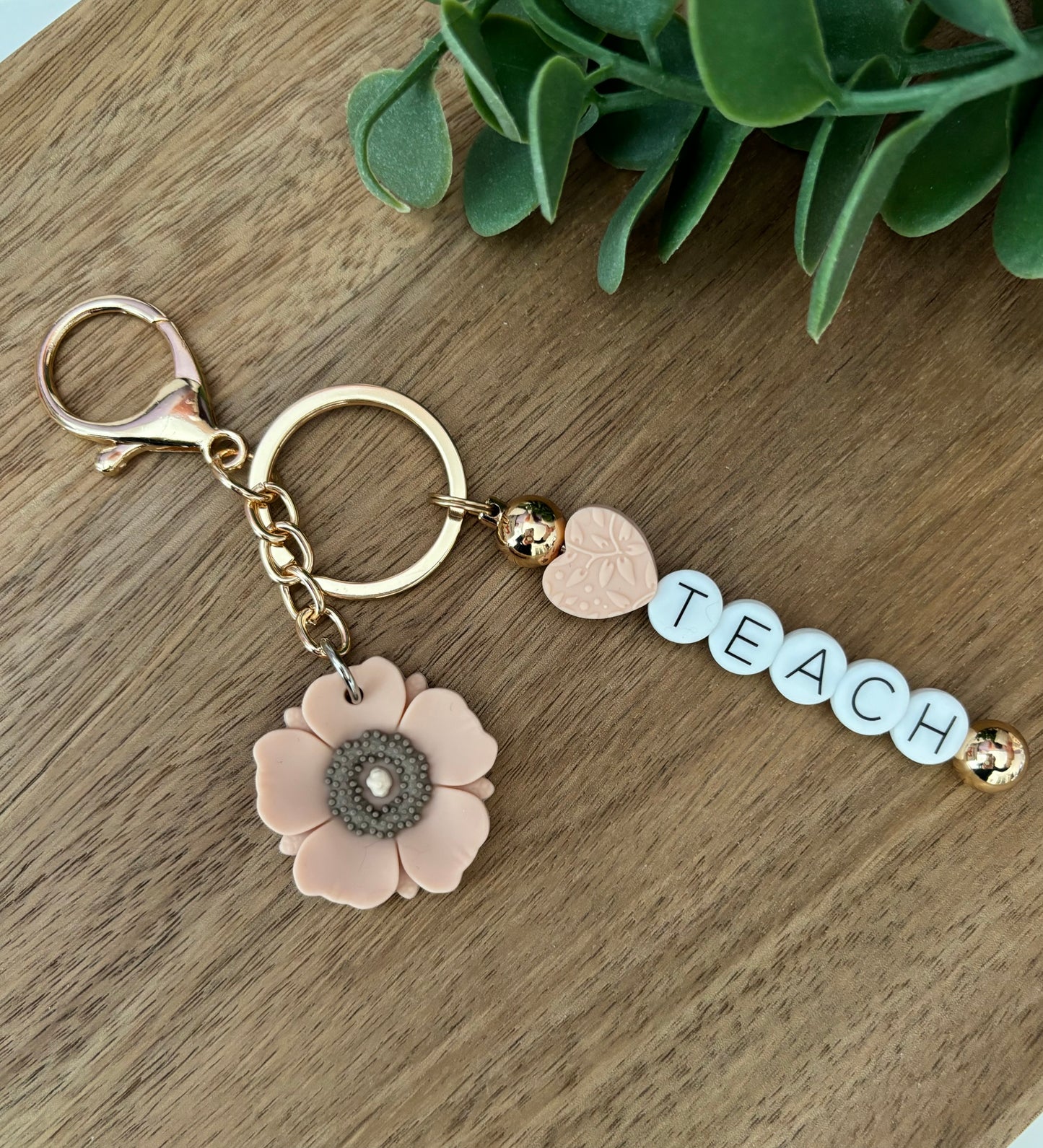 A keychain with a floral design and the word 'Teach' written on it, displayed on a wooden surface.