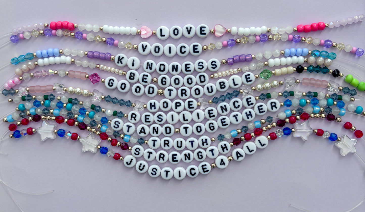 11 beaded bracelets with peaceful resistance words on a light purple background.  LOVE. VOICE. KINDNESS. BE GOOD. GOOD TROUBLE. HOPE. RESILIENCE. STAND TOGETHER. TRUTH. STRENGTH. JUSTICE FOR ALL.