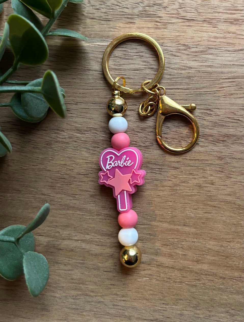 Keychain with pink heart and 'Barbie' logo on a wooden surface