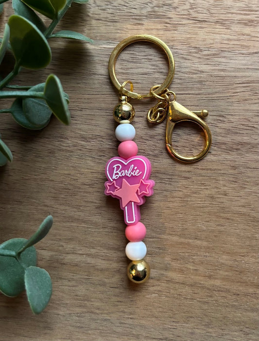 Keychain with pink heart and 'Barbie' logo on a wooden surface