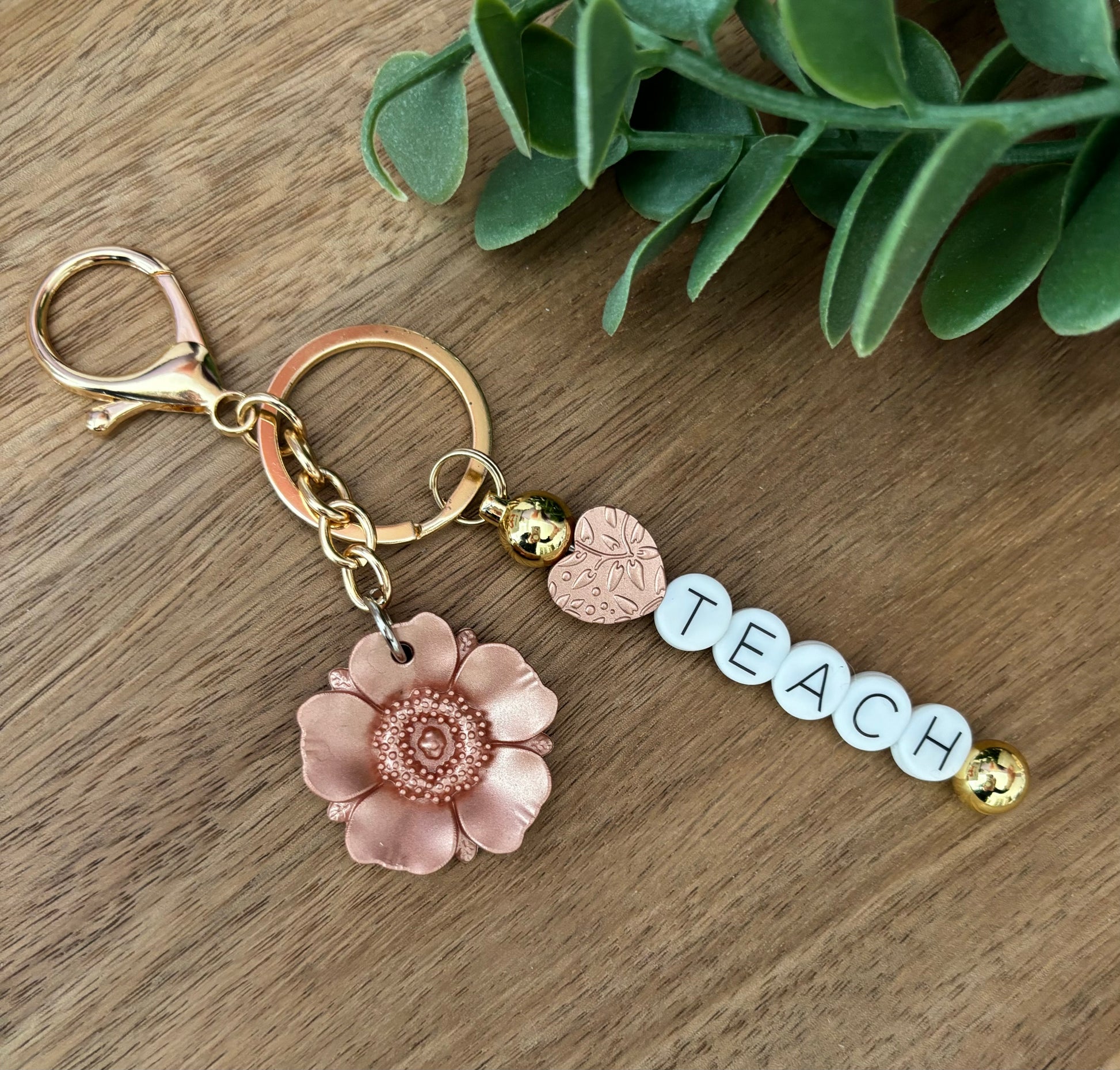 A keychain with a floral design and the word 'Teach' written on it, displayed on a wooden surface.