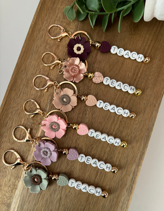 A collection of keychains with floral designs and the word 'Teach' written on them, displayed on a wooden surface.