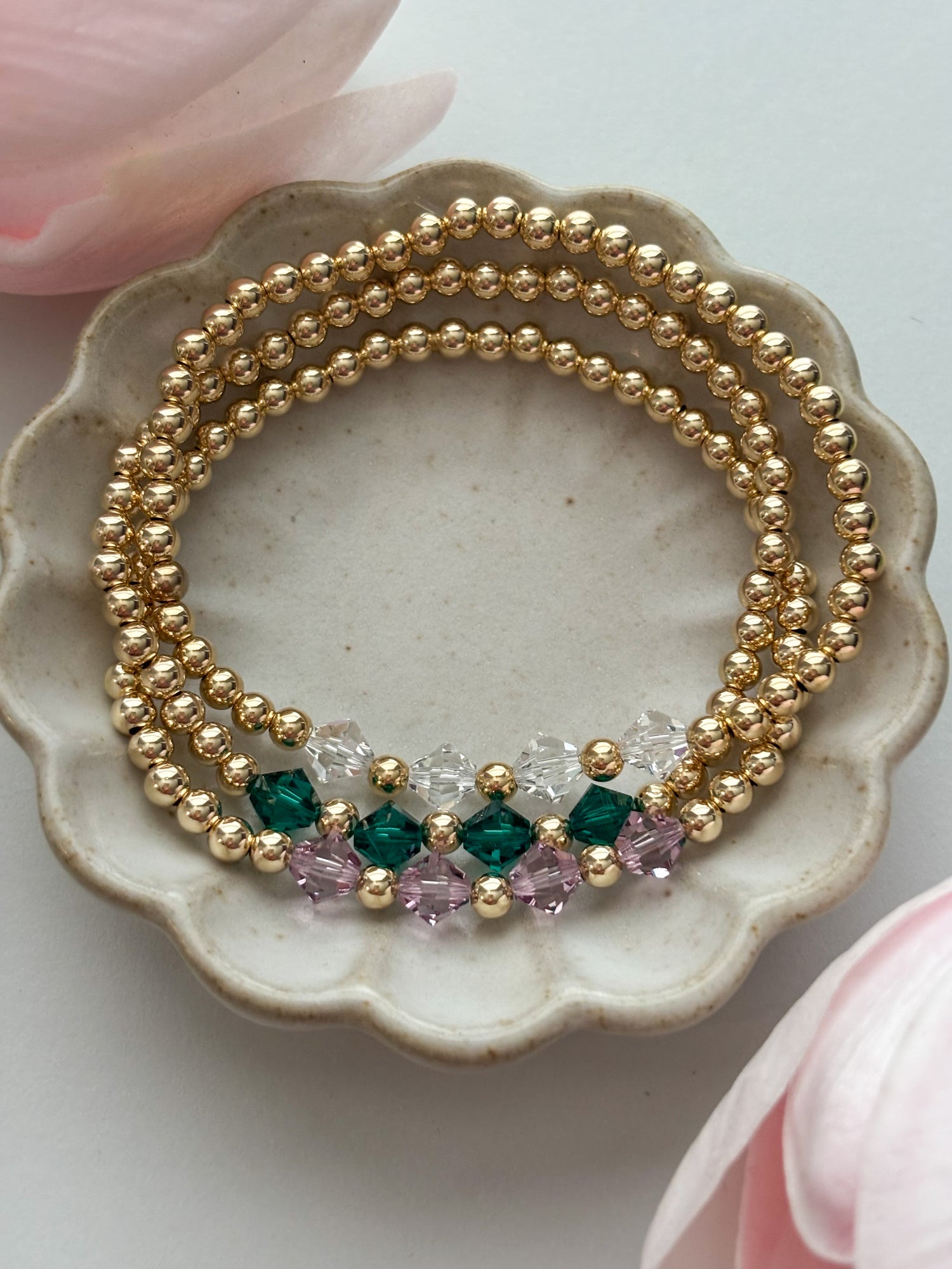 Three gold beaded bracelets with colored beads on a decorative plate.