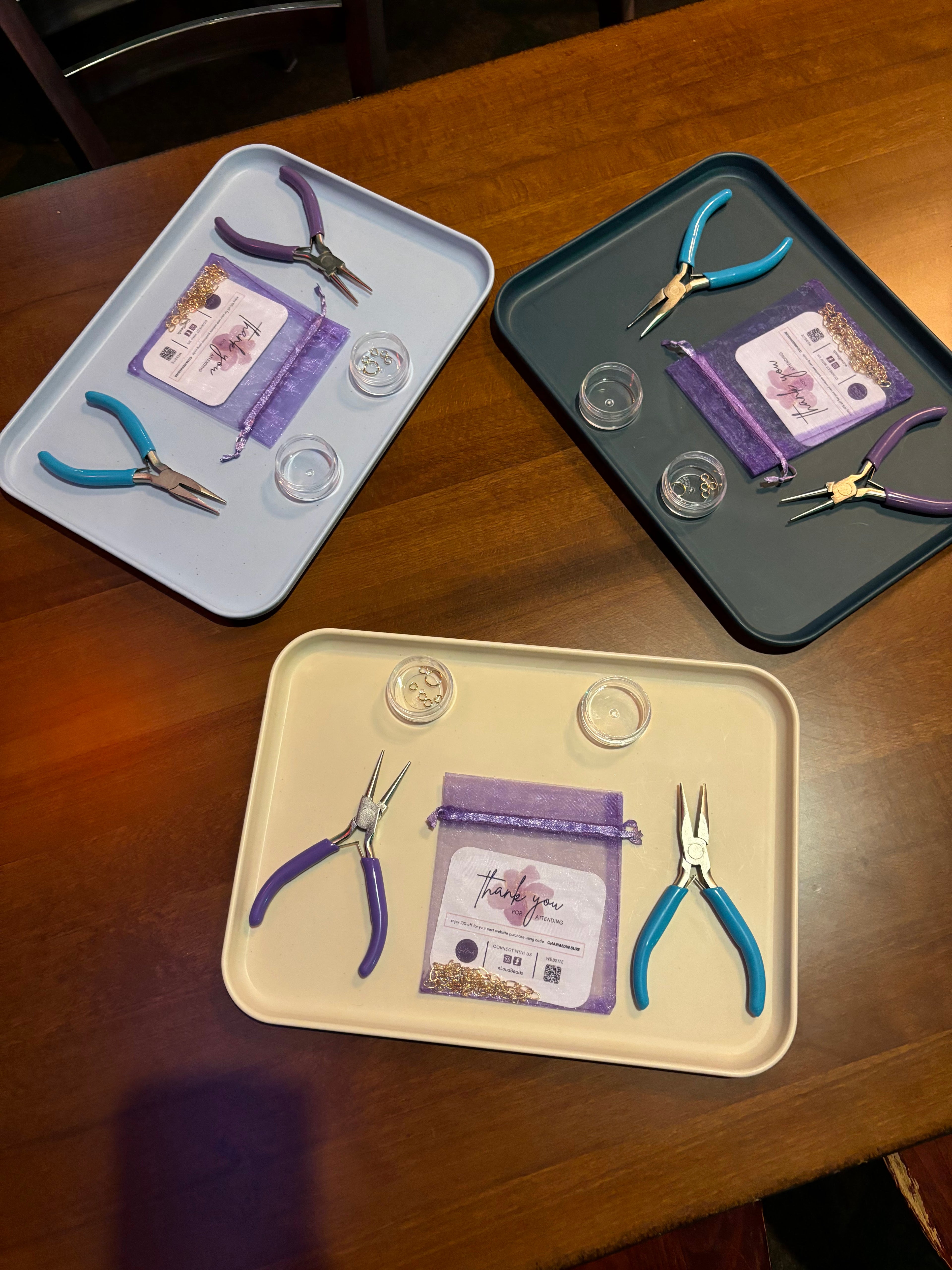 Three trays with jewelry-making tools and supplies on a wooden surface