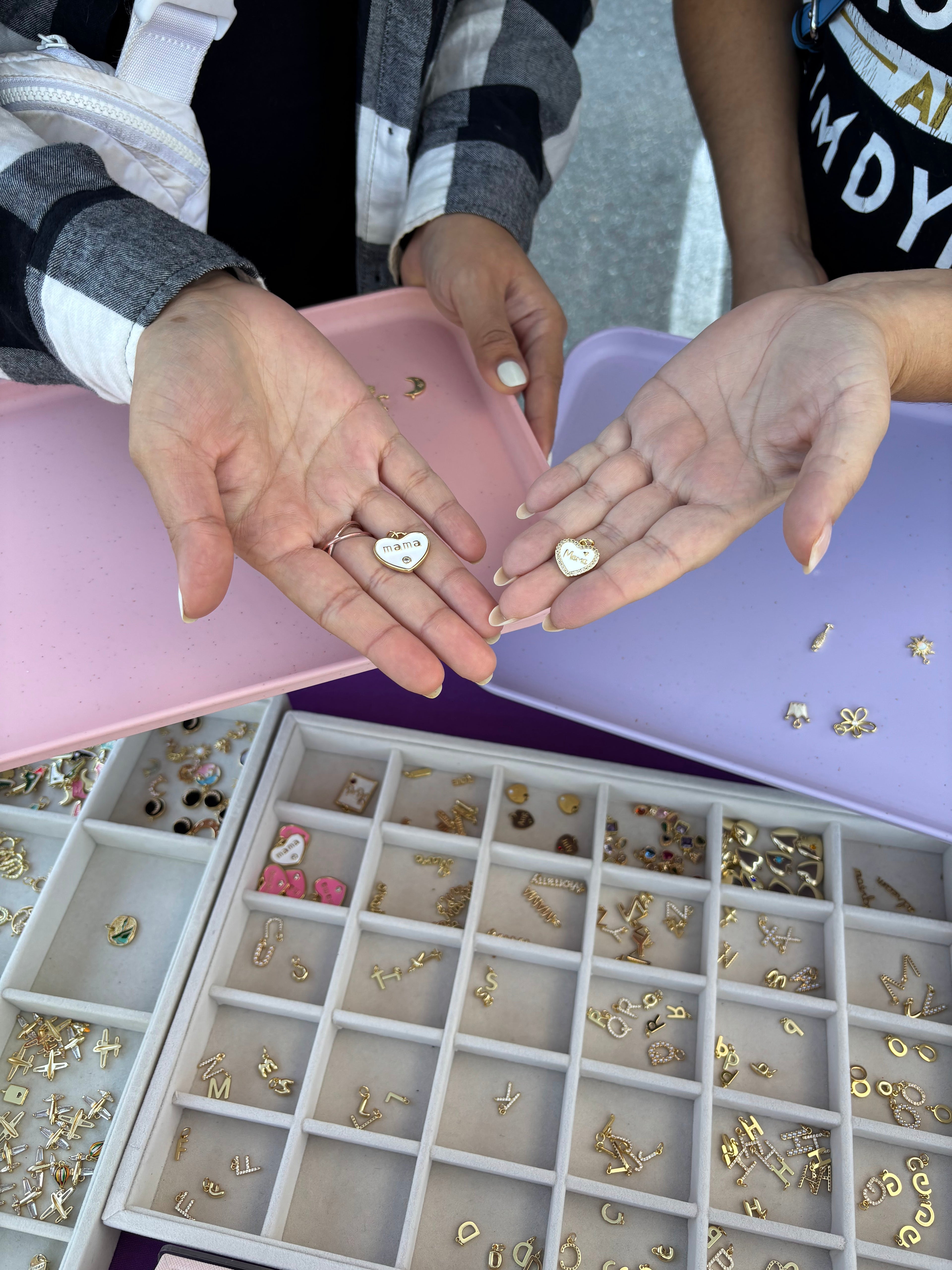 Two pairs of hands holding small gold jewelry pieces above a tray with more jewelry.