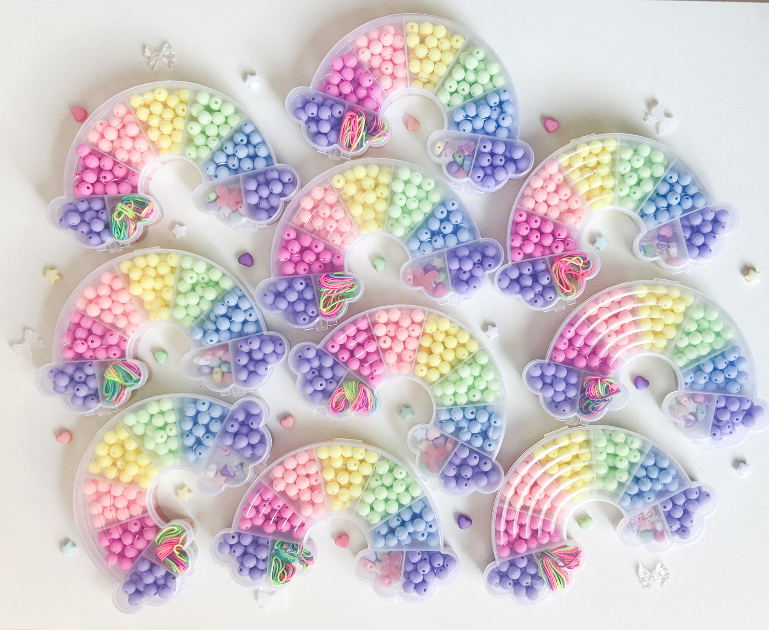 A collection of rainbow shaped bead kits with pastel beads inside them and around them on a light background.