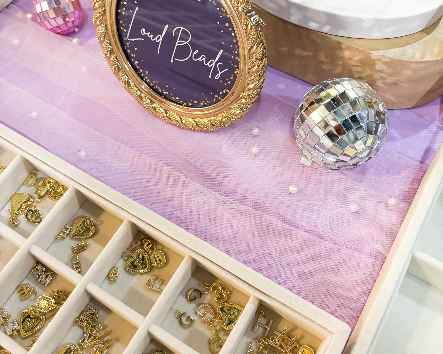 Jewelry display with gold earrings, a decorative frame, and a 'Loud Beads' sign on a purple mat.