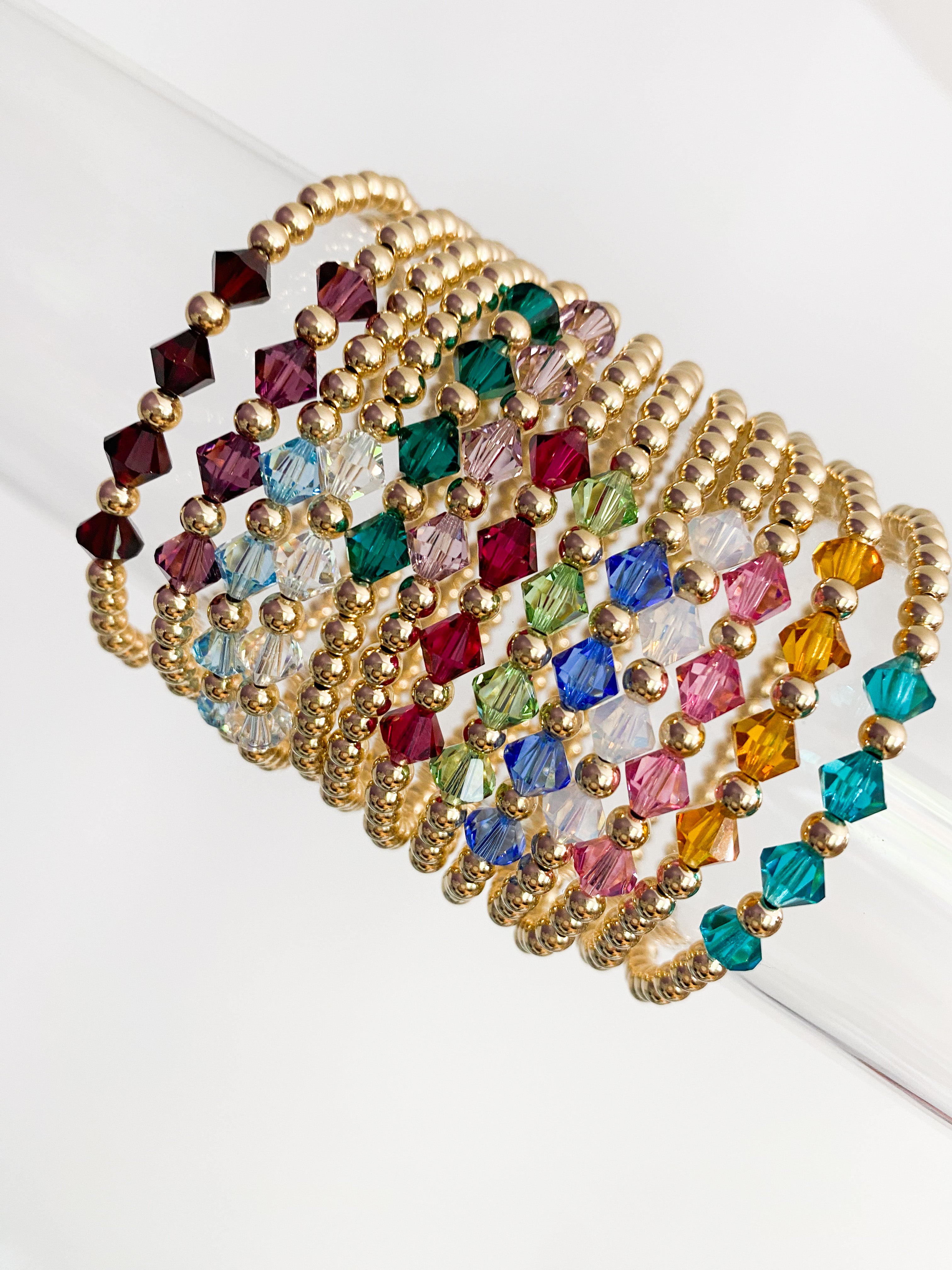 A multicolored beaded bracelet with gold-filled beads and Swarovski crystals, displayed on a transparent strand.