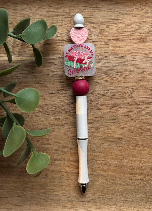 Decorative pen with a red bead on a wooden surface with green leaves.