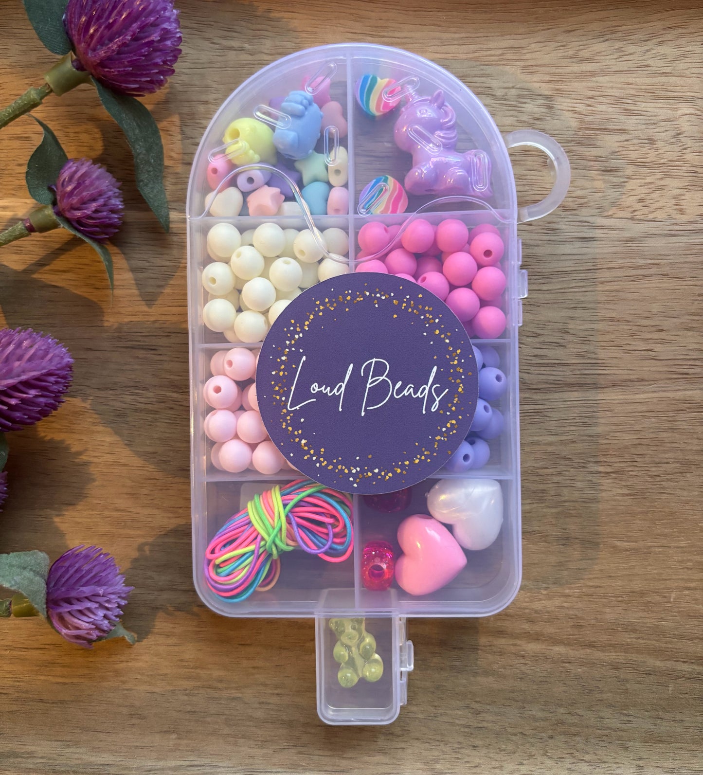 Clear popsicle shaped container with colorful beads on a wooden surface