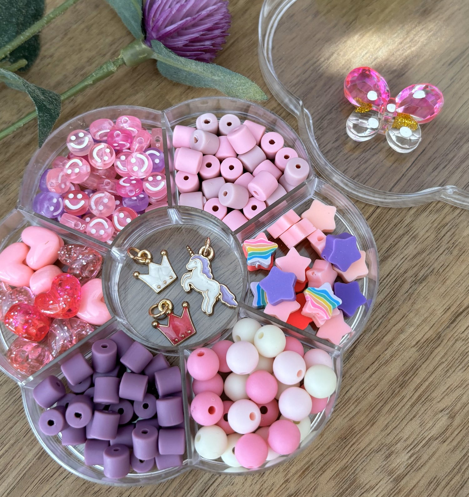 Colorful bead set in a clear plastic organizer on a wooden surface with decorative elements.