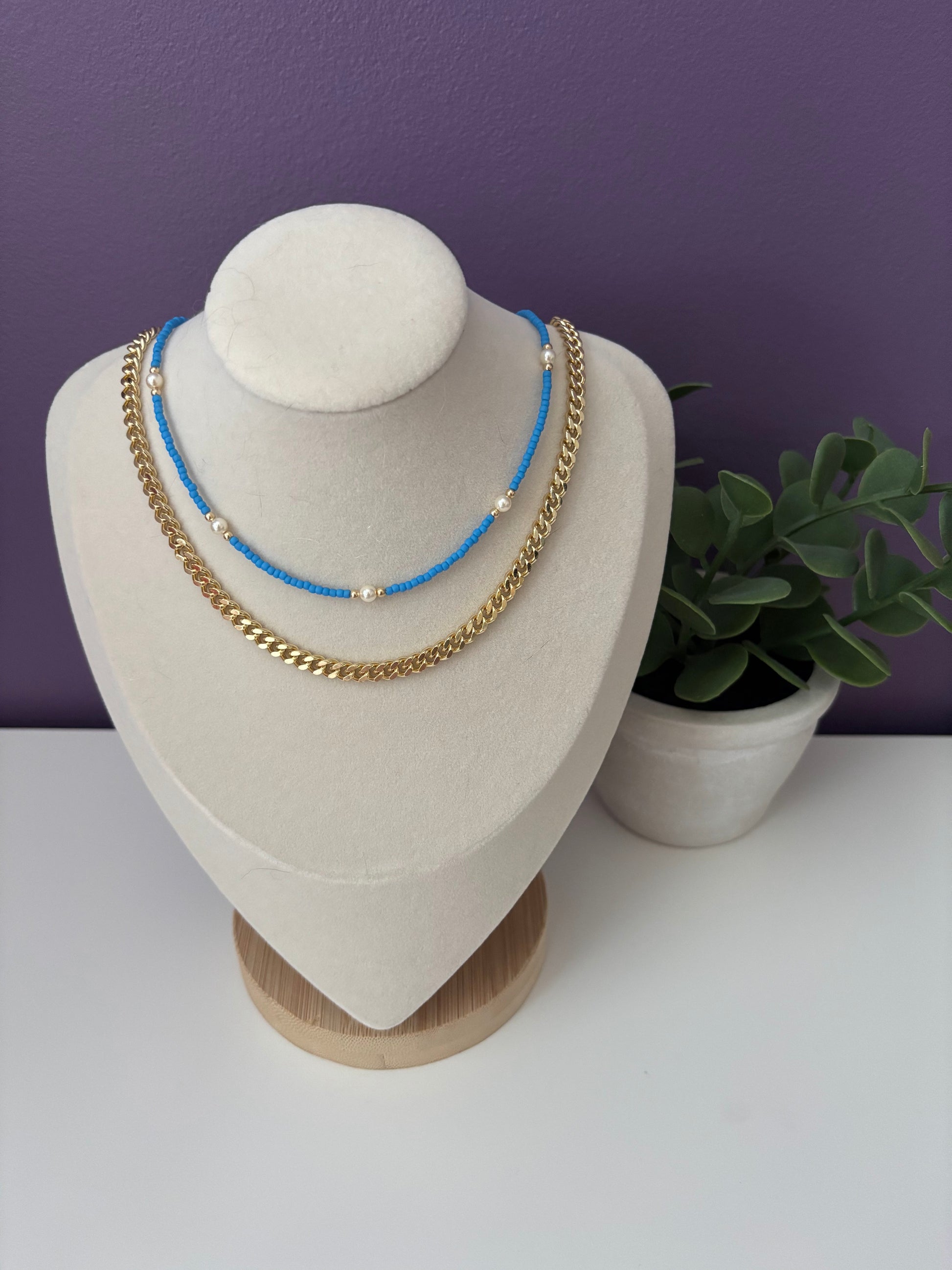 Necklaces on a mannequin bust with a purple wall and plant in the background