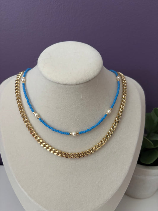 Two necklaces on a white bust against a purple background