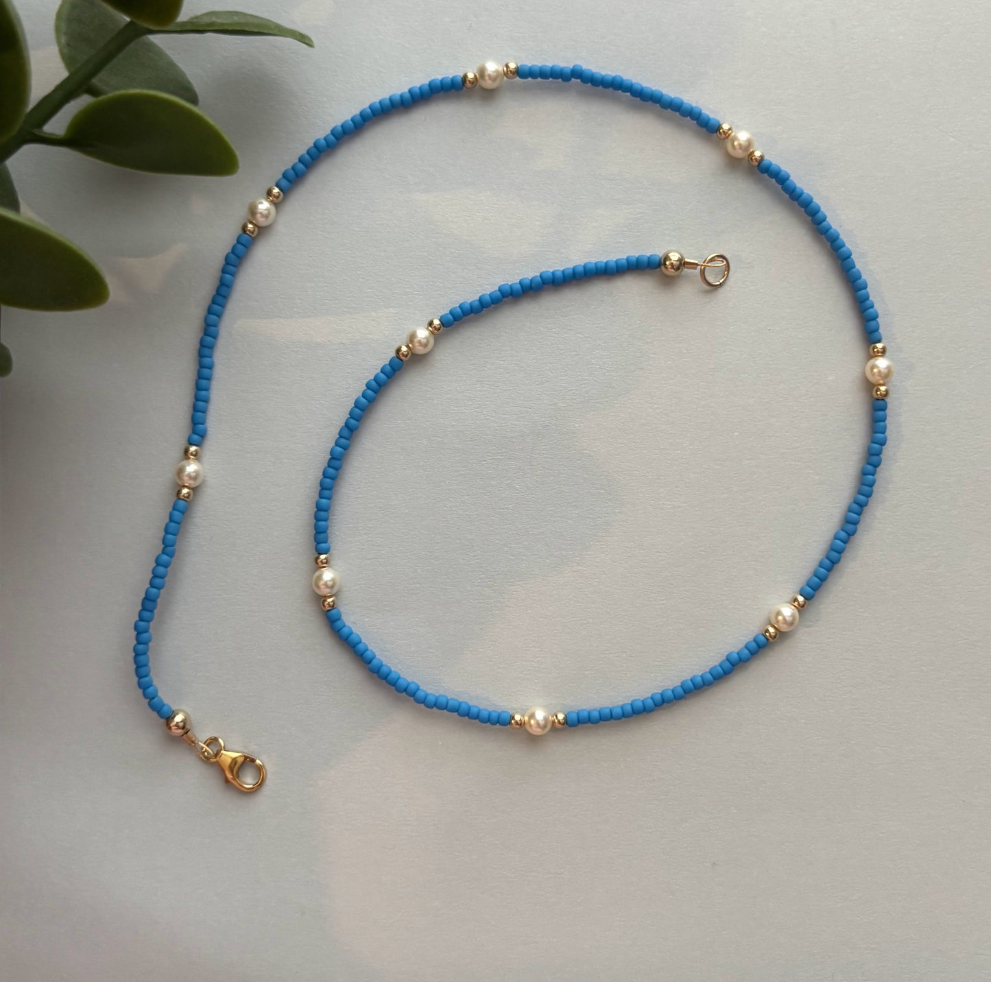 Blue beaded necklace with gold accents on a light gray surface