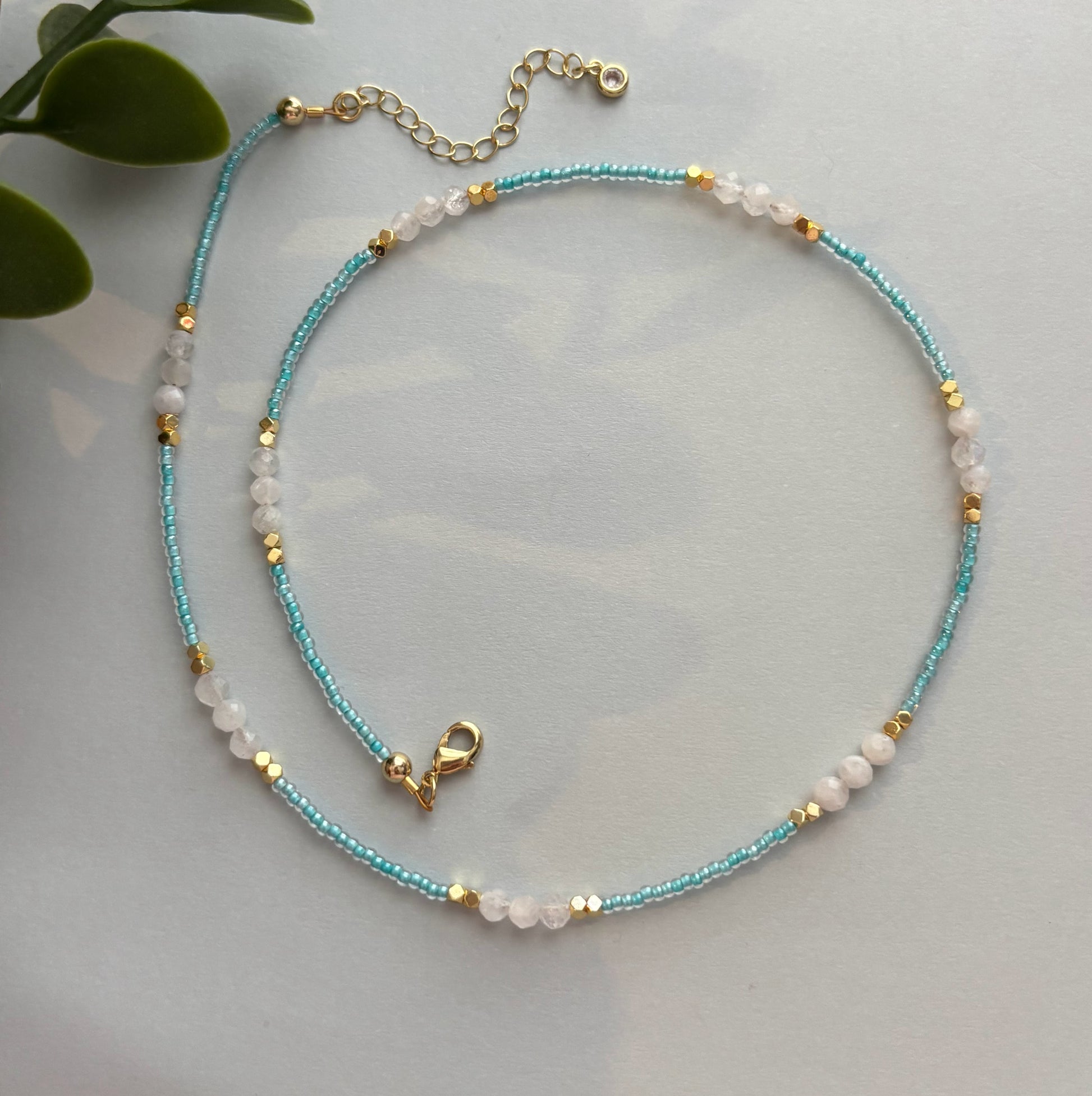 Beaded necklace with blue and gold accents on a light gray background