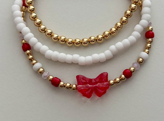 Three layered bracelets with red and gold beads on a light gray background