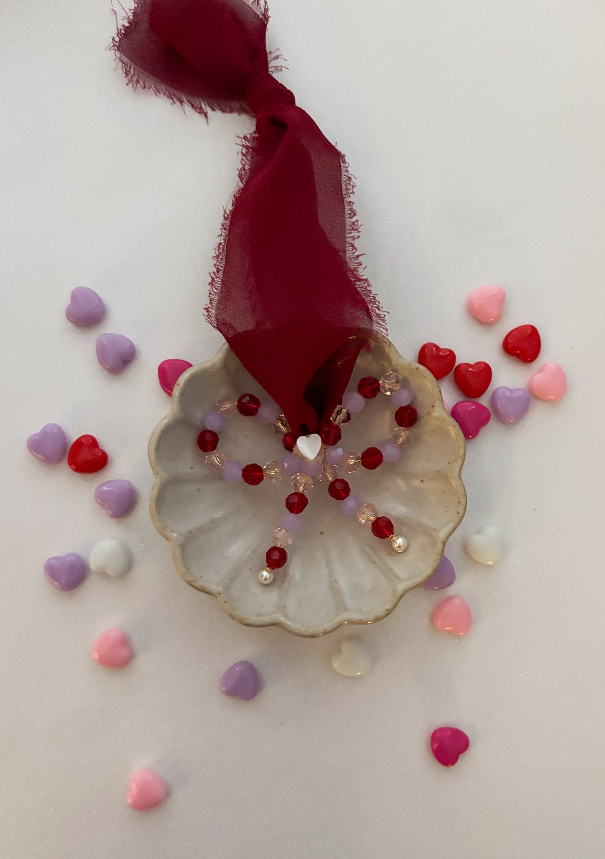 Decorative bow ornament with a red ribbon and heart-shaped beads on a white background