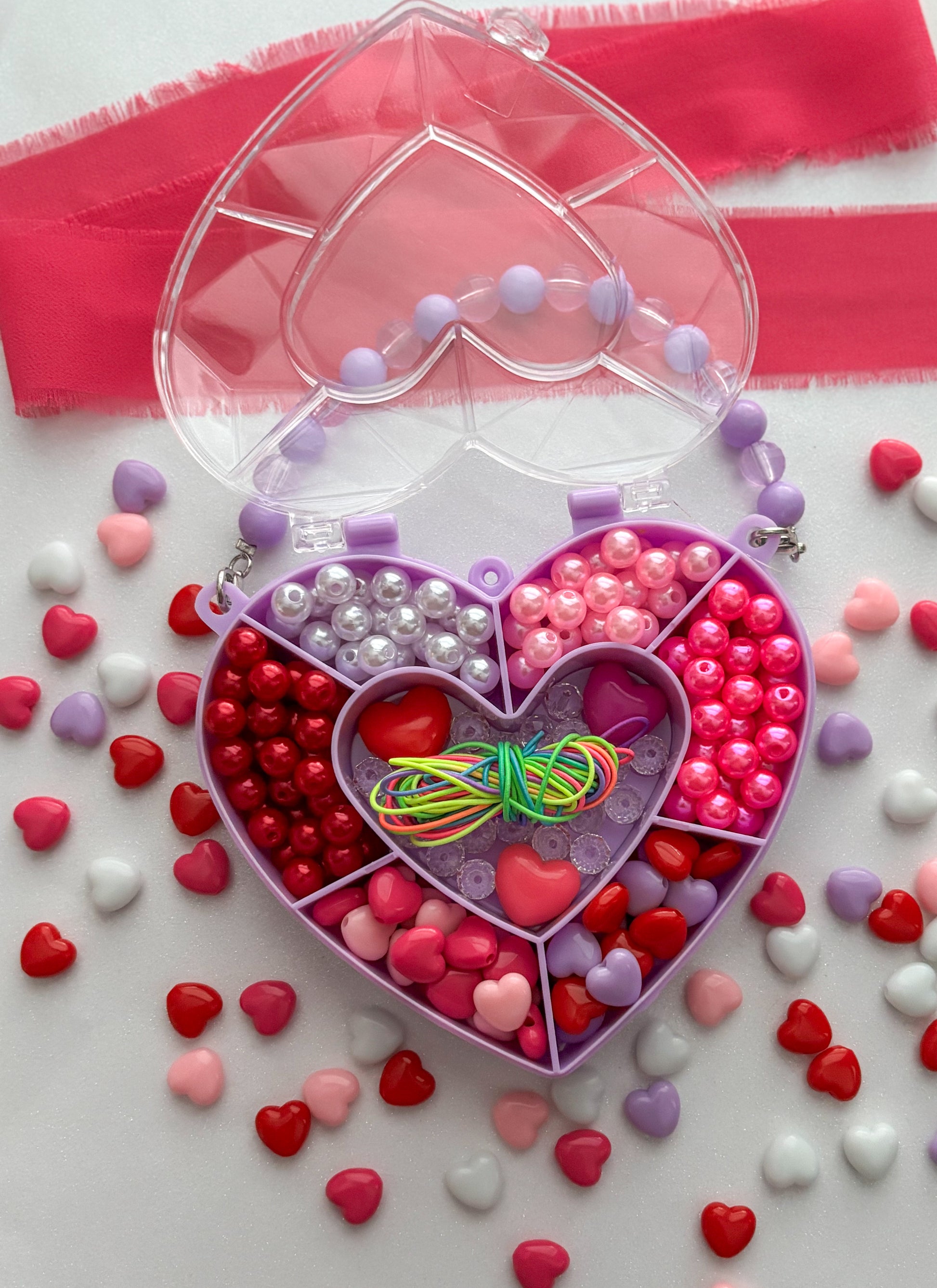 Heart-shaped bead kit with beads and ribbons on a white background