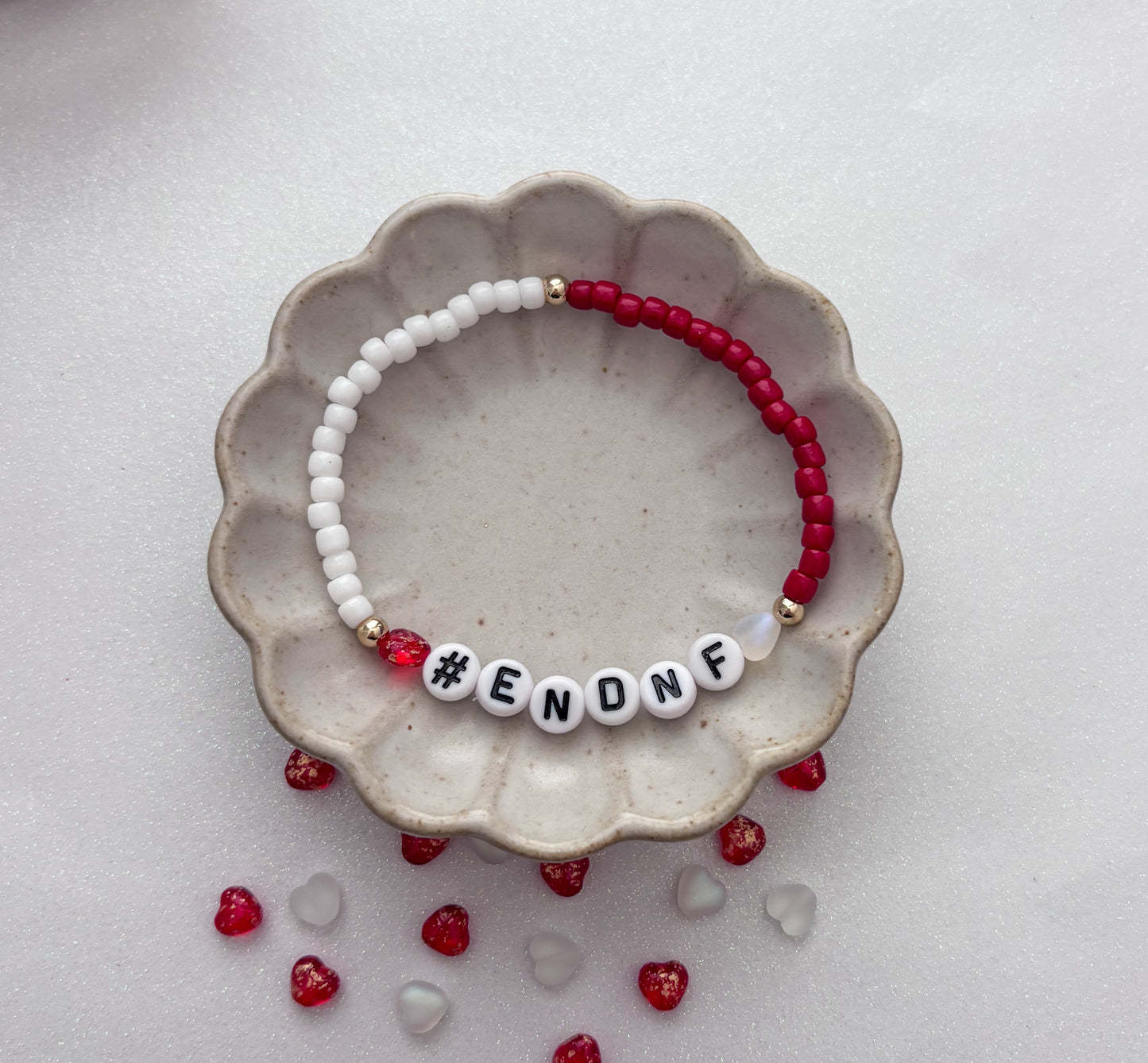 Beaded bracelet with '#ENONF' on a ceramic dish with red and clear beads.
