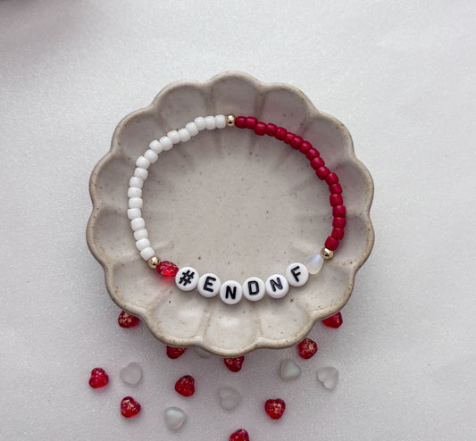 Beaded bracelet with '#ENONF' on a ceramic dish with red and clear beads.