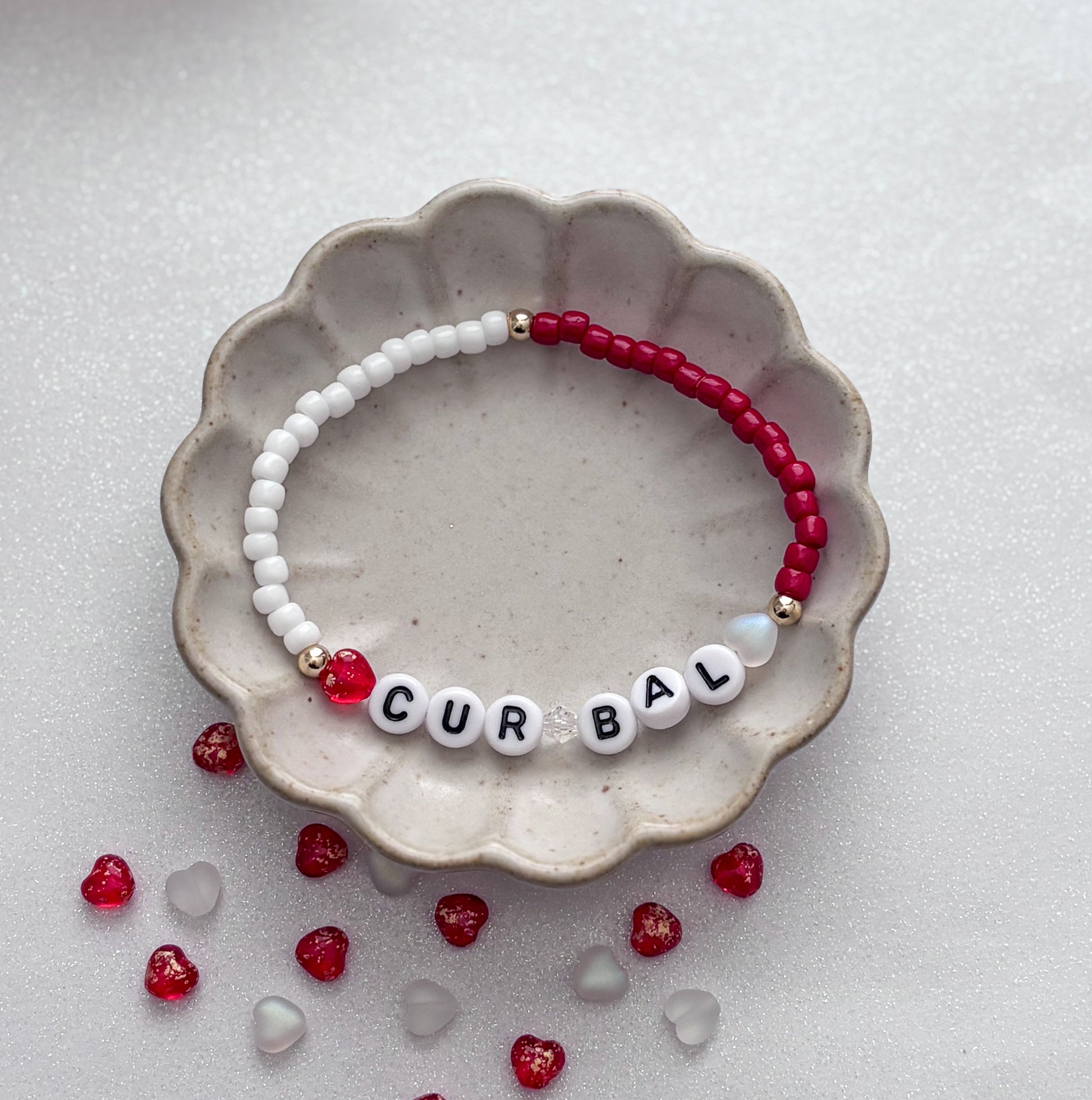 Beaded bracelet with letter beads spelling 'CURBAL' on a textured surface with scattered beads.