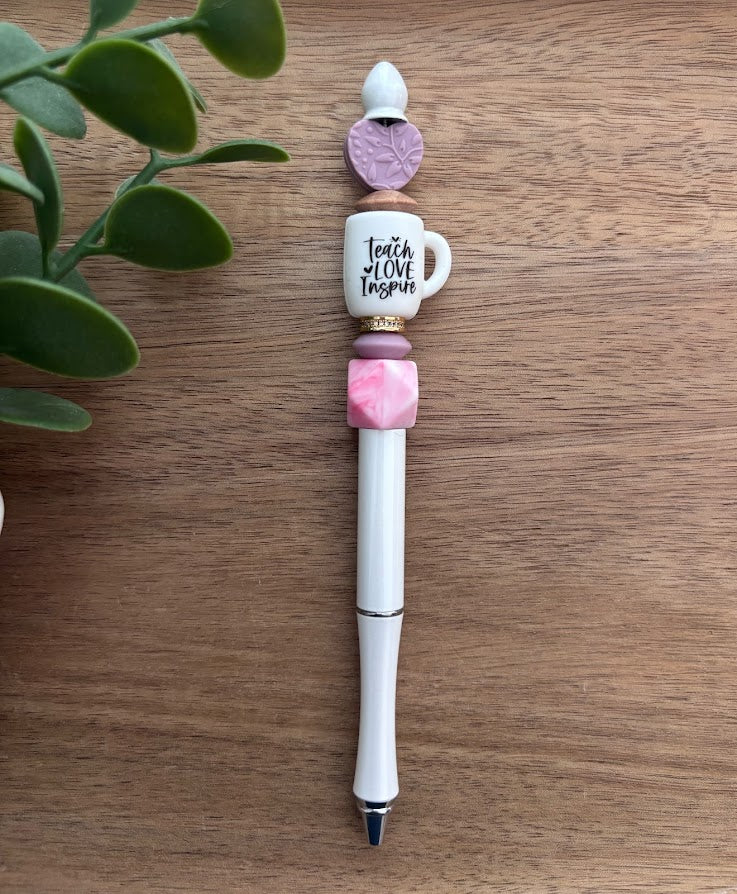 Decorative pen with beads and a small mug charm on a wooden surface