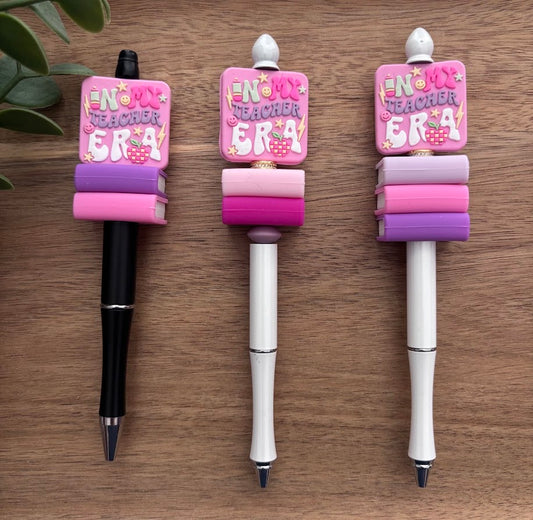 Three decorative pens with pink and purple accents on a wooden surface.